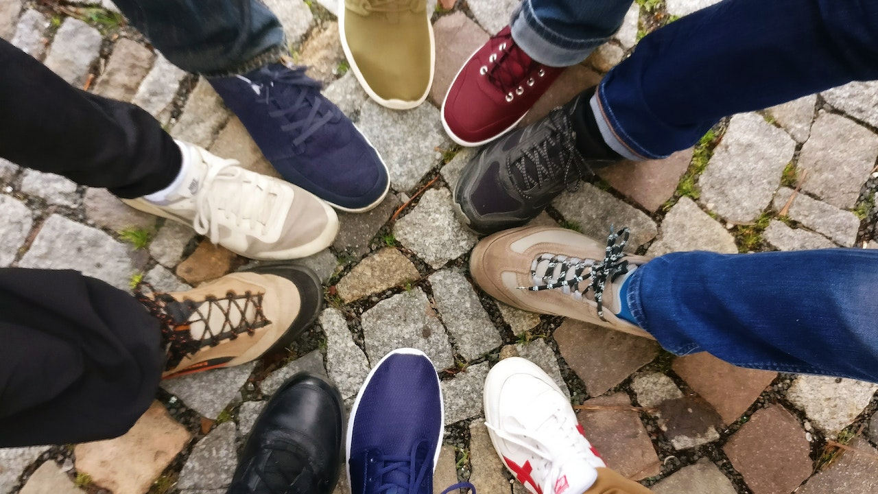 10 different feet with different shoes form a circle on a stone floor.